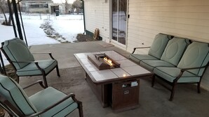 Une terrasse avec une table autour d’un foyer, deux chaises et un canapé.