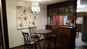 Une cuisine avec coin repas, comprenant un lustre, un grand tableau représentant des fleurs, des meubles de rangement en bois et un réfrigérateur.