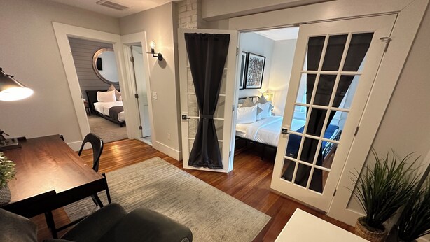 A modern living room with a dining area, a bedroom with a large window, and a hallway leading to another room.