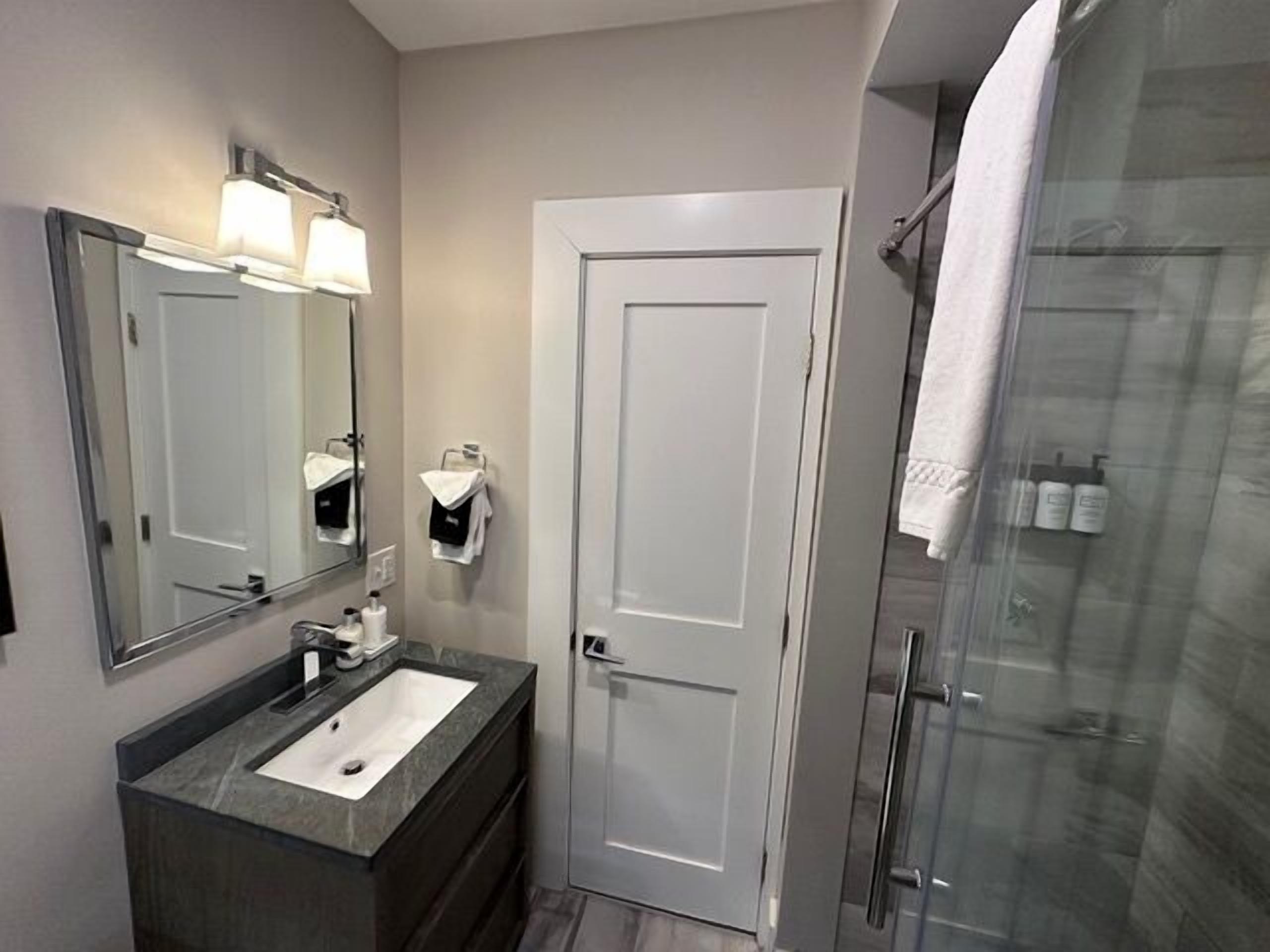 A modern bathroom with a large mirror, a sink, a towel rack, and a glass shower enclosure.