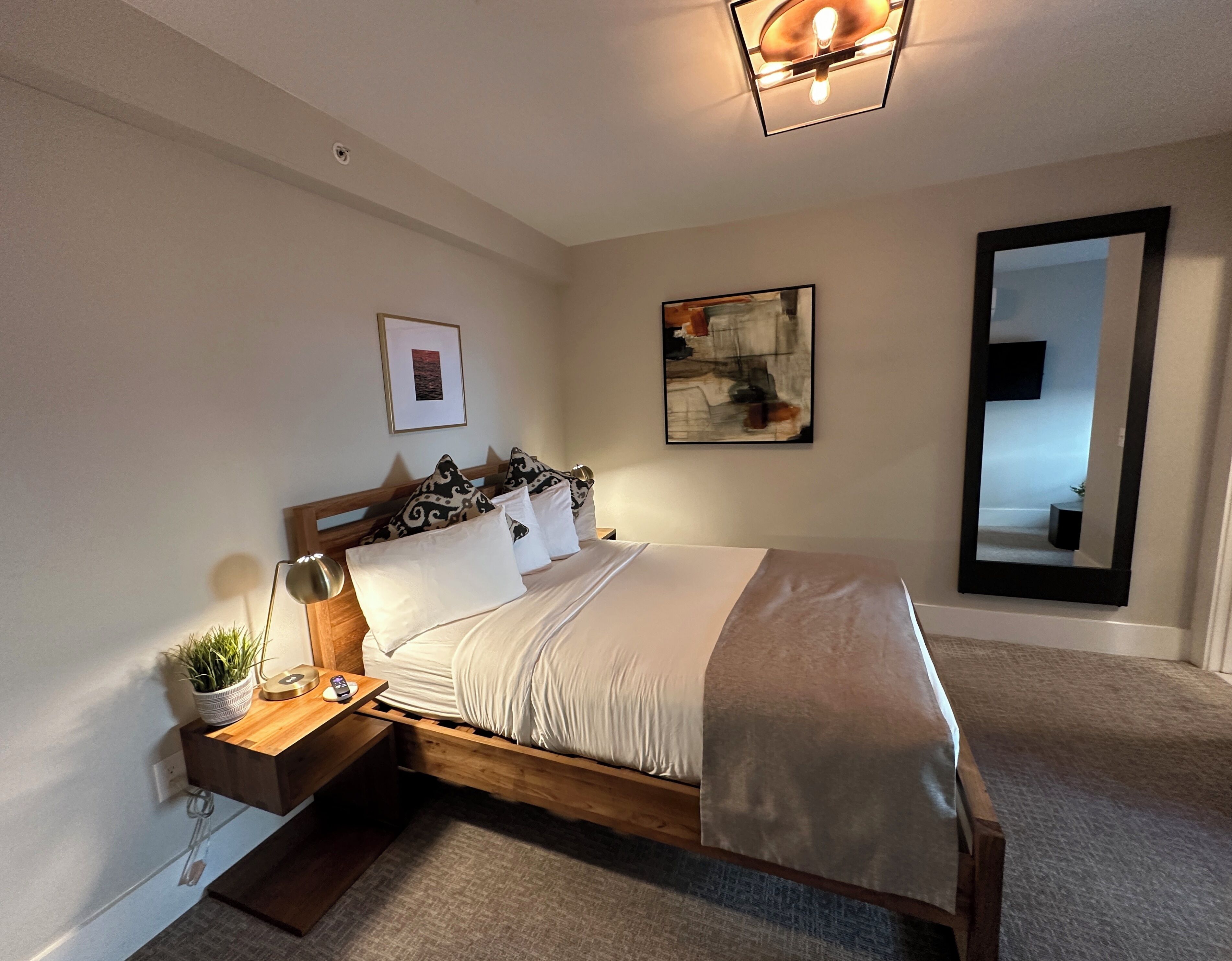 A neatly arranged bedroom with a wooden bed, bedside tables, a nightstand, a wall-mounted TV, and a large mirror.