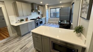 A modern kitchen with grey cabinets, a stainless steel range hood, and a large island with a sink.