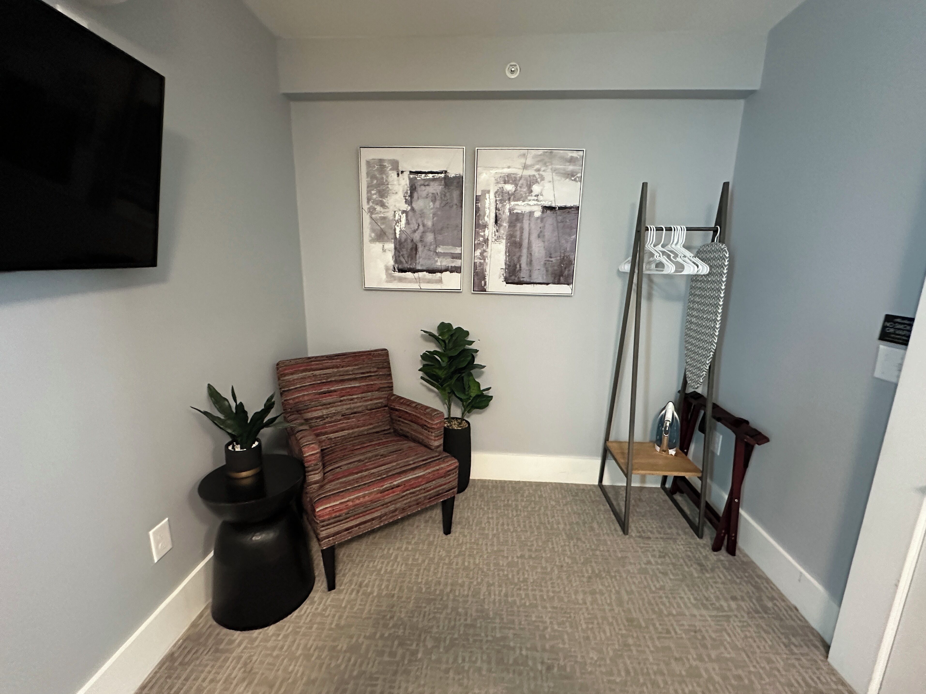 A living room with a flat-screen TV, two abstract paintings, a striped armchair, a potted plant, and a wooden bench.