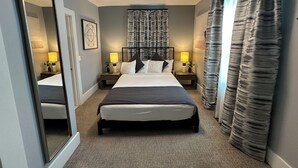 Una habitación de hotel con una cama grande, dos mesitas de noche con lámparas, una lámpara de techo y un espejo amplio.