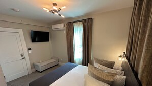 Ein Hotelzimmer mit einem Bett, einem Fernseher, einer Klimaanlage, einer Bank und einem Fenster mit Vorhängen.