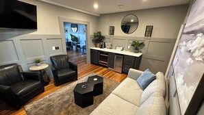 Un salon moderne comprenant un canapé, des fauteuils, une table basse et un coin cuisine avec un réfrigérateur et un plan de travail.