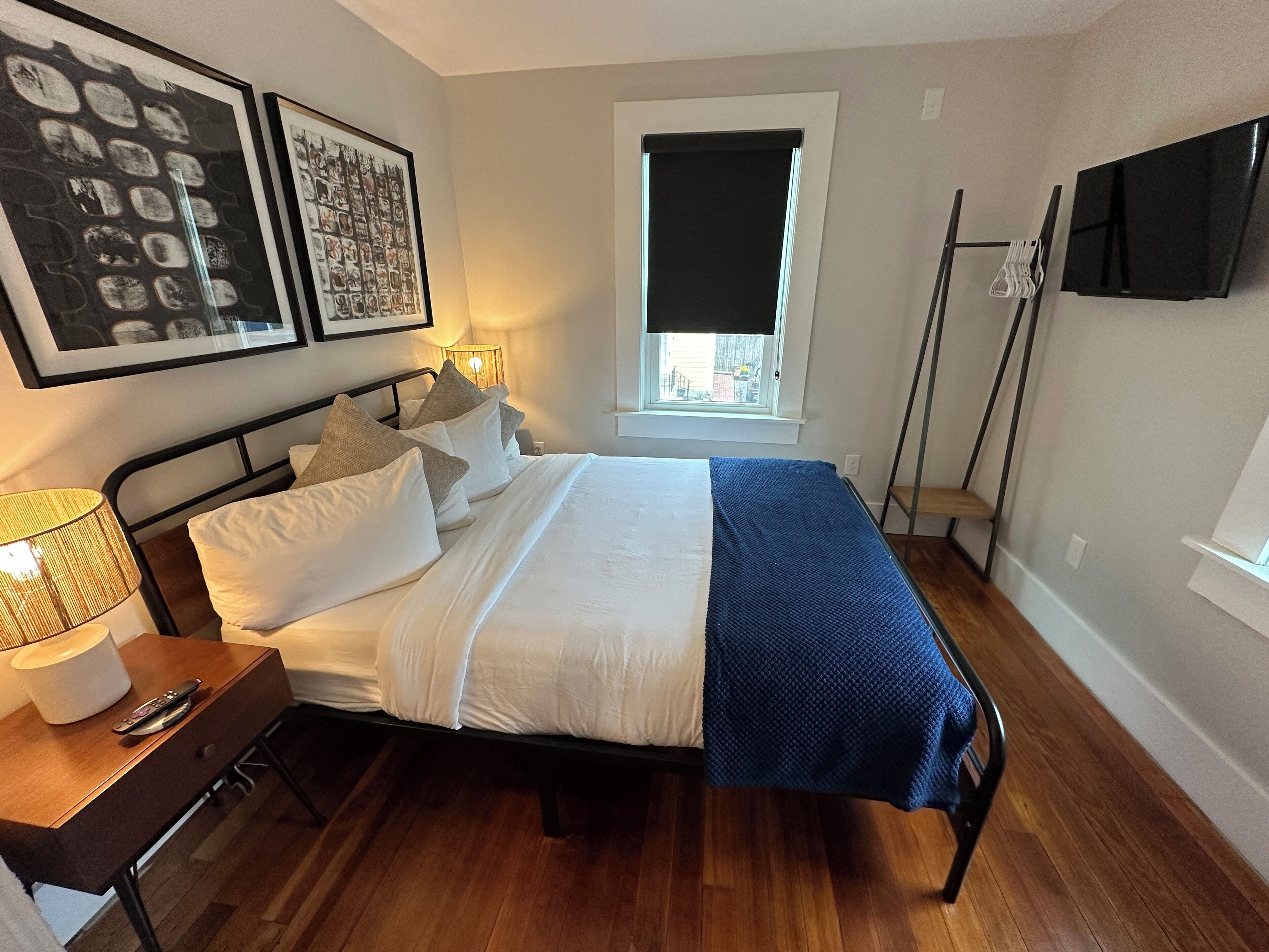 A neatly arranged bedroom with a bed, bedside table, lamp, and artwork on the wall.