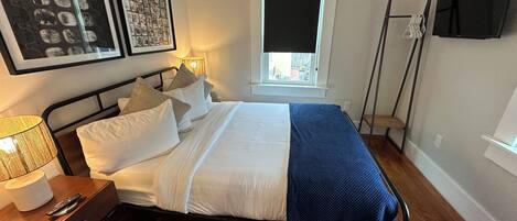 A neatly arranged bedroom with a bed, bedside table, lamp, and artwork on the wall.