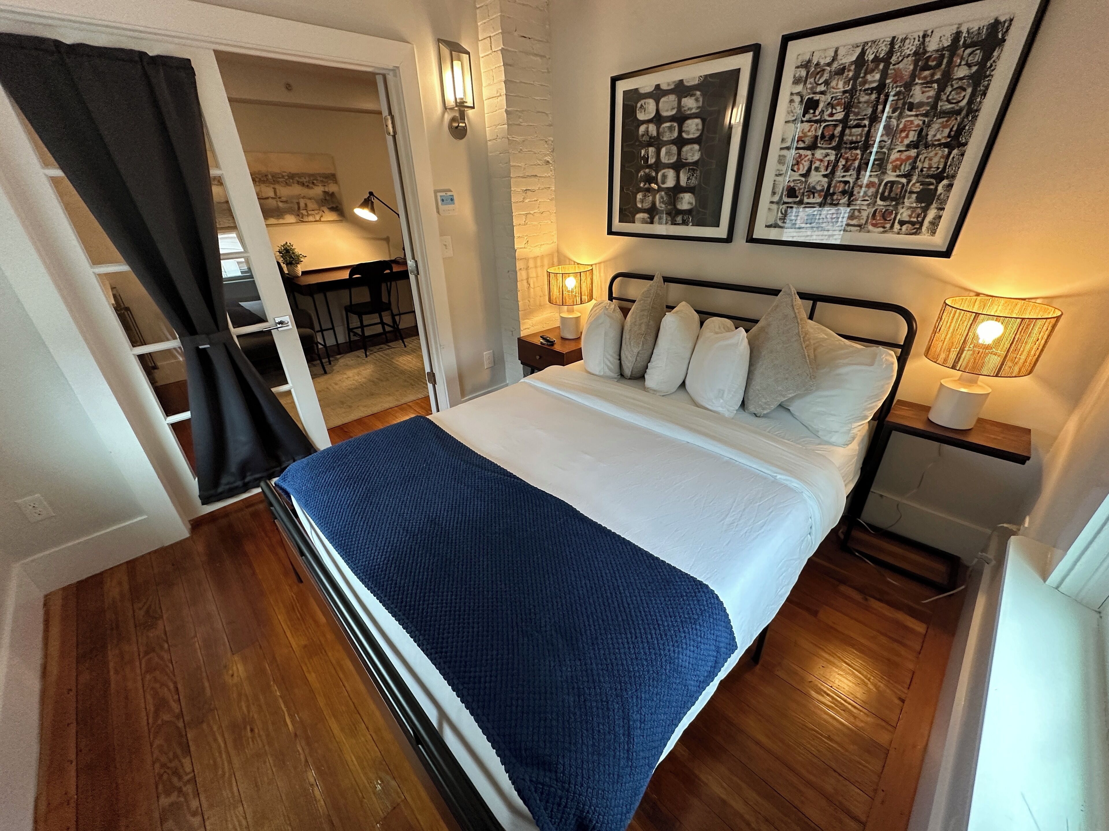 A bedroom with a bed, two bedside tables, a nightstand, a lamp, and a wall-mounted light fixture.