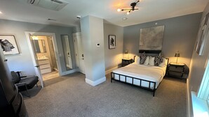 A bedroom with a large bed, bedside tables, a ceiling fan, and a bathroom with a shower and sink.