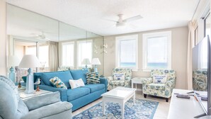 Una sala de estar con un sofá azul, dos sillones, una mesa de centro y un televisor.