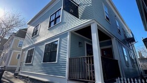 A two-story house with a front porch and a mailbox. - Spacious and modern 1 Bed/ 1 Bath / (Sleeps 4)  Dog friendly with parking on Historic Pelham St. (Newport)
