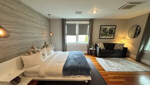 Une chambre moderne avec un grand lit, un canapé, une petite table et une fenêtre avec des rideaux.