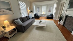 Ein geräumiges Wohnzimmer mit grauem Sofa, weißem Couchtisch und Kamin.