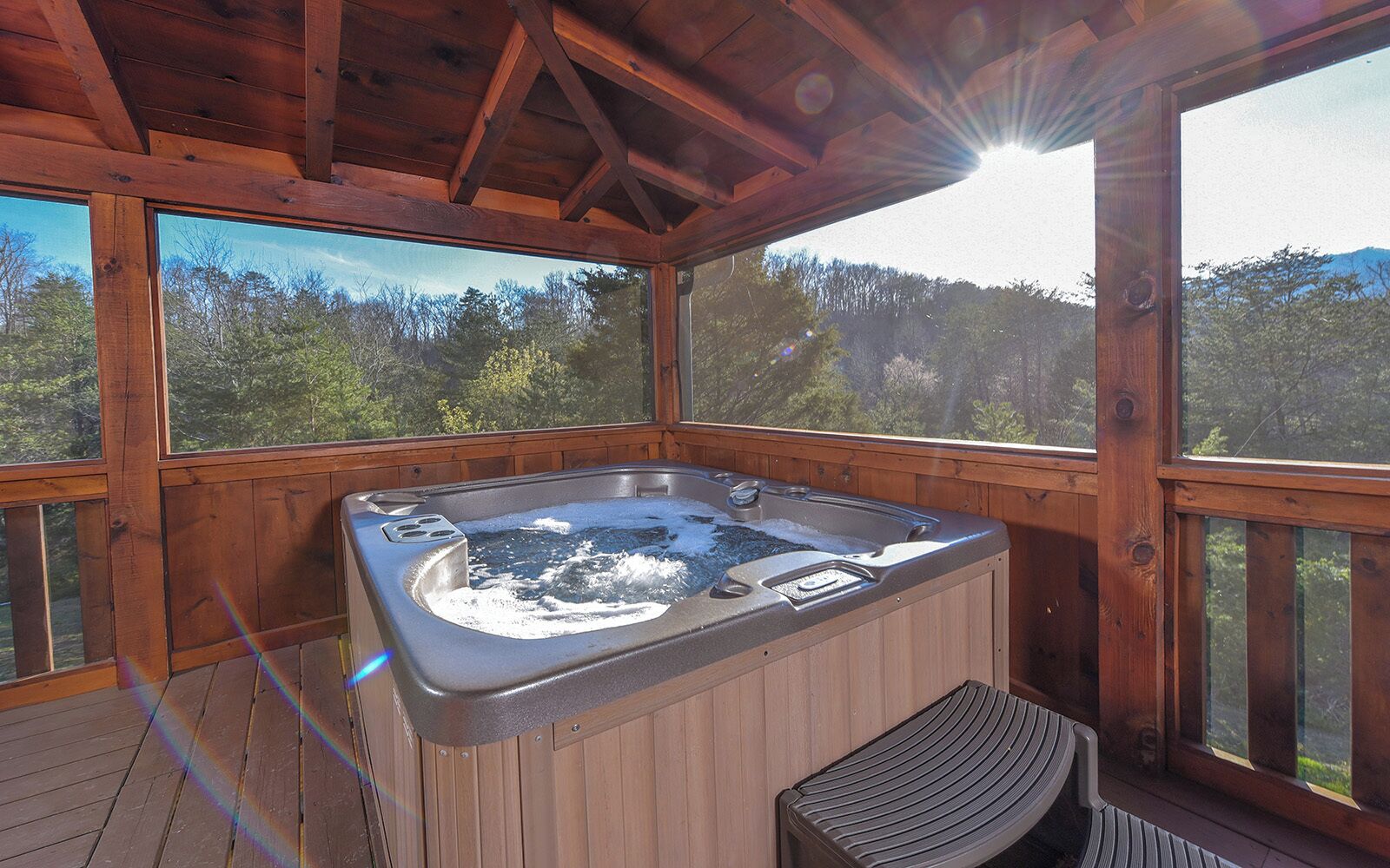 A wooden hot tub with a view of a forested landscape.