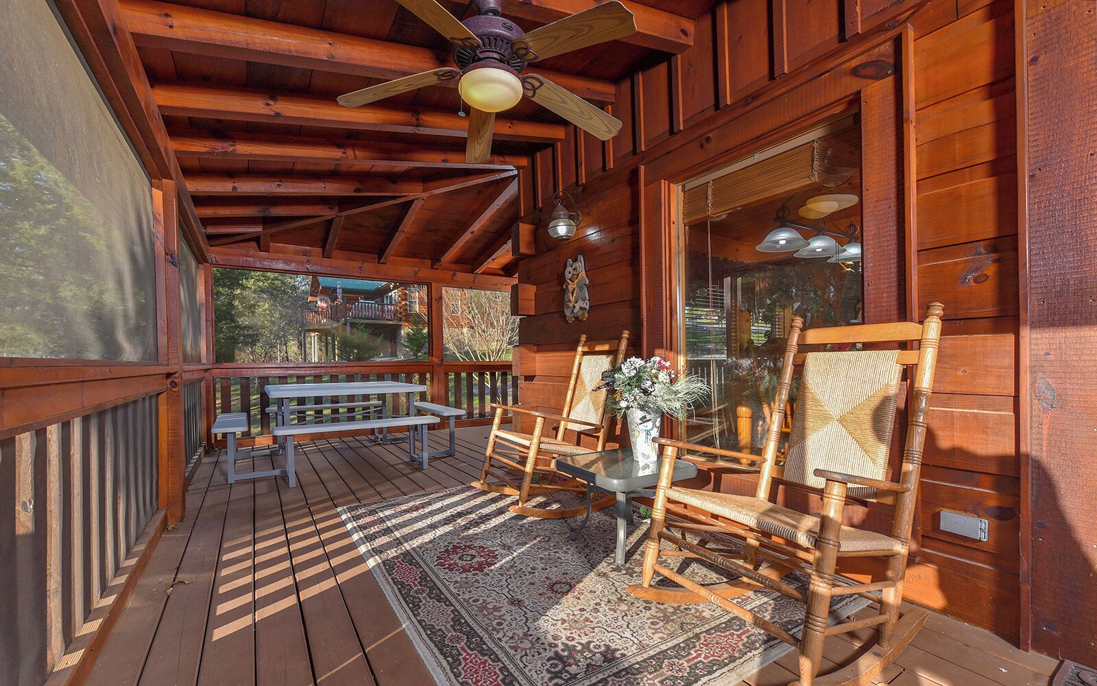Una terraza de madera con una mesa, sillas, un ventilador de techo y una ventana con vista a un edificio.