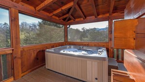 Una cabaña de madera con jacuzzi, ventanas amplias y vistas al bosque.