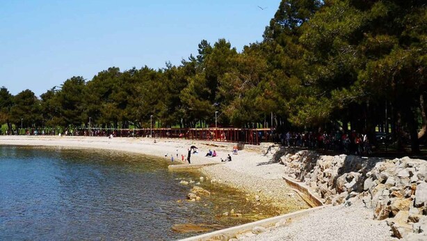 Uma praia com águas cristalinas, costa rochosa e árvores densas ao fundo.