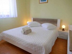 Un lit bien fait, avec une couette blanche, deux oreillers et une serviette enroulée posée sur le lit. Il y a deux tables de chevet avec des lampes, une de chaque côté du lit.
