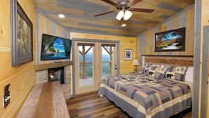 A cozy bedroom with a stone fireplace, a large bed with a quilt, a television, and a ceiling fan. - Theater, Games & Views! - Bigger Bear Views Lodge (Gatlinburg)