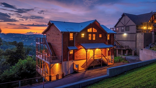 A log cabin with a balcony and a staircase leading to a deck, surrounded by a scenic landscape. - Theater, Games & Views! - Bigger Bear Views Lodge (Gatlinburg)
