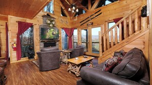 A cozy log cabin interior with a fireplace, leather furniture, and a scenic view. - My Runaway Wagon Retreat - Hot Tub & Mountain View (Sevierville)
