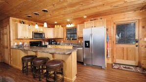 A wooden cabin-style kitchen with a central island, bar stools, stainless steel appliances, and wooden cabinets. - My Runaway Wagon Retreat - Hot Tub & Mountain View (Sevierville)