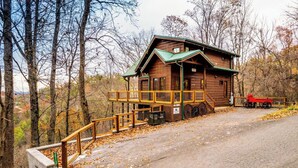 A wooden cabin with a green roof, a covered porch, and a red tractor parked outside. - My Runaway Wagon Retreat - Hot Tub & Mountain View (Sevierville)
