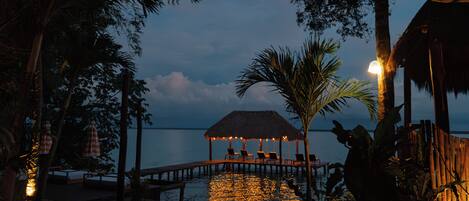 A wooden deck with lounge chairs, a thatched-roof structure, and a view of the water.