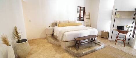 A bedroom with a bed, bedside table, lamp, and a small wooden bench.