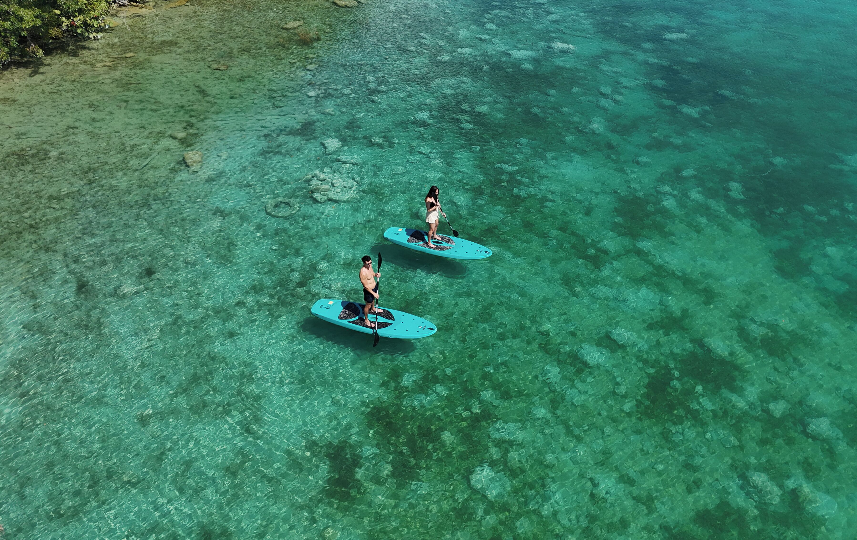 Deux personnes pratiquent le paddle sur une eau turquoise.