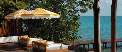 A wooden deck with lounge chairs and striped umbrellas overlooking a body of water.