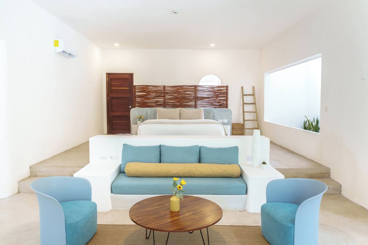 Un salon moderne comprenant un canapé, deux fauteuils, une table basse et un escalier menant à une chambre.
