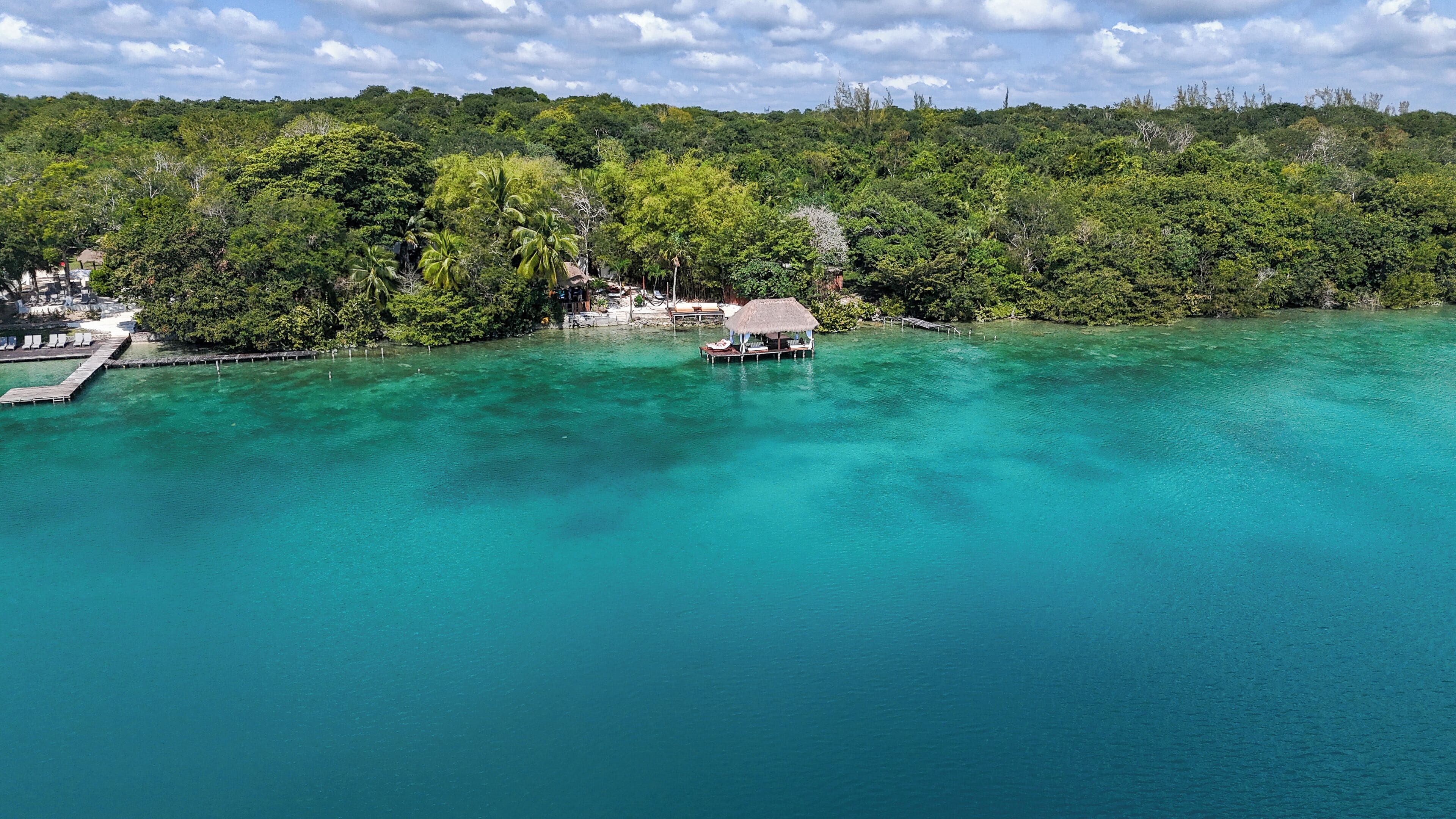 A tropical resort with a clear turquoise lagoon, a thatched-roof hut, and lush greenery.