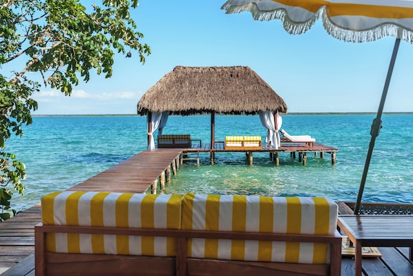 A wooden deck with a thatched-roof hut, wooden lounge chairs, and a small table.
