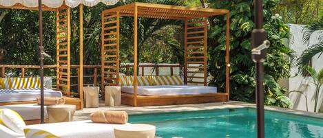 A poolside area with wooden cabanas, lounge chairs, and a clear blue pool.