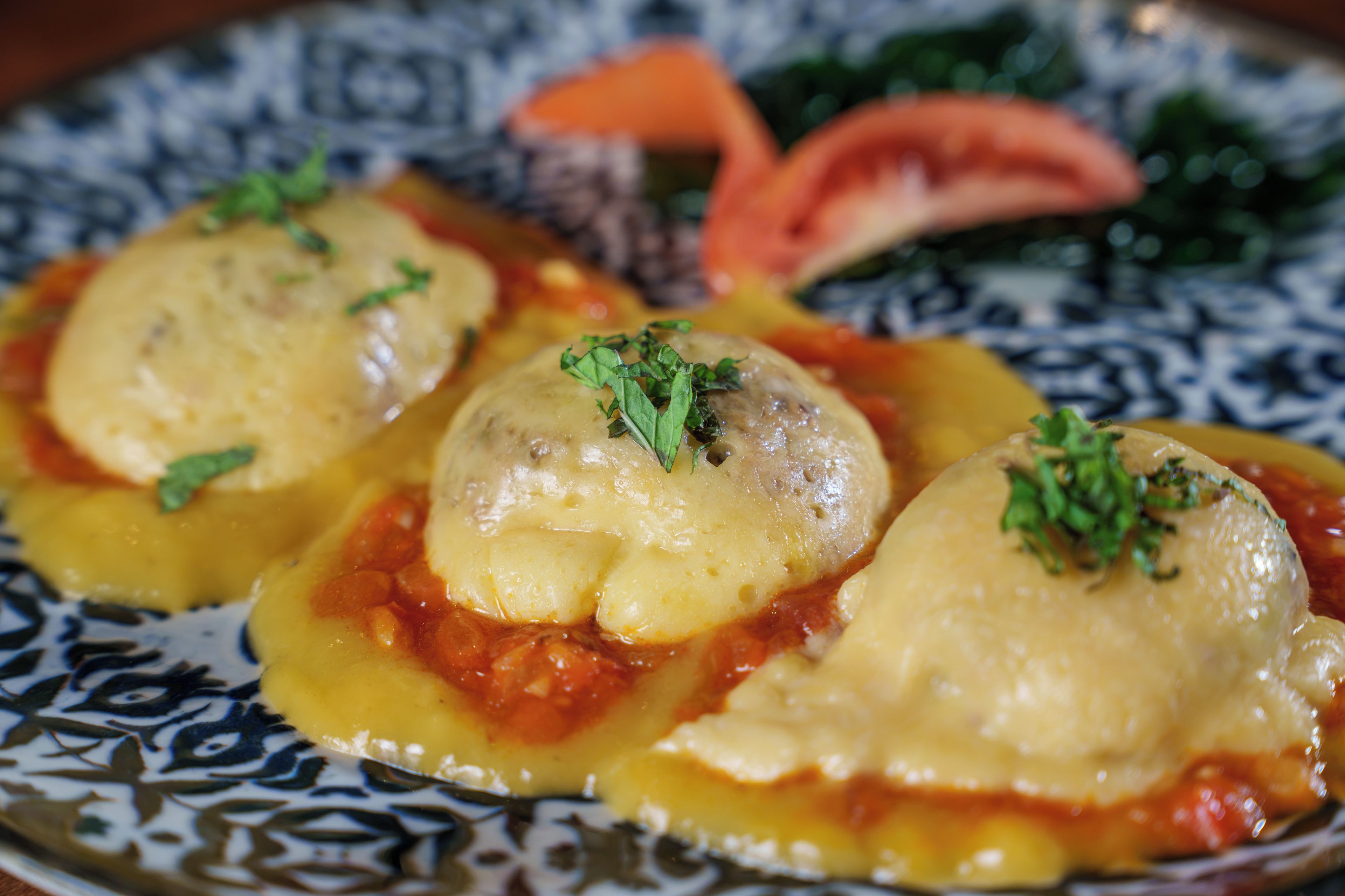 A plate of ravioli with a tomato-based sauce and garnished with herbs.