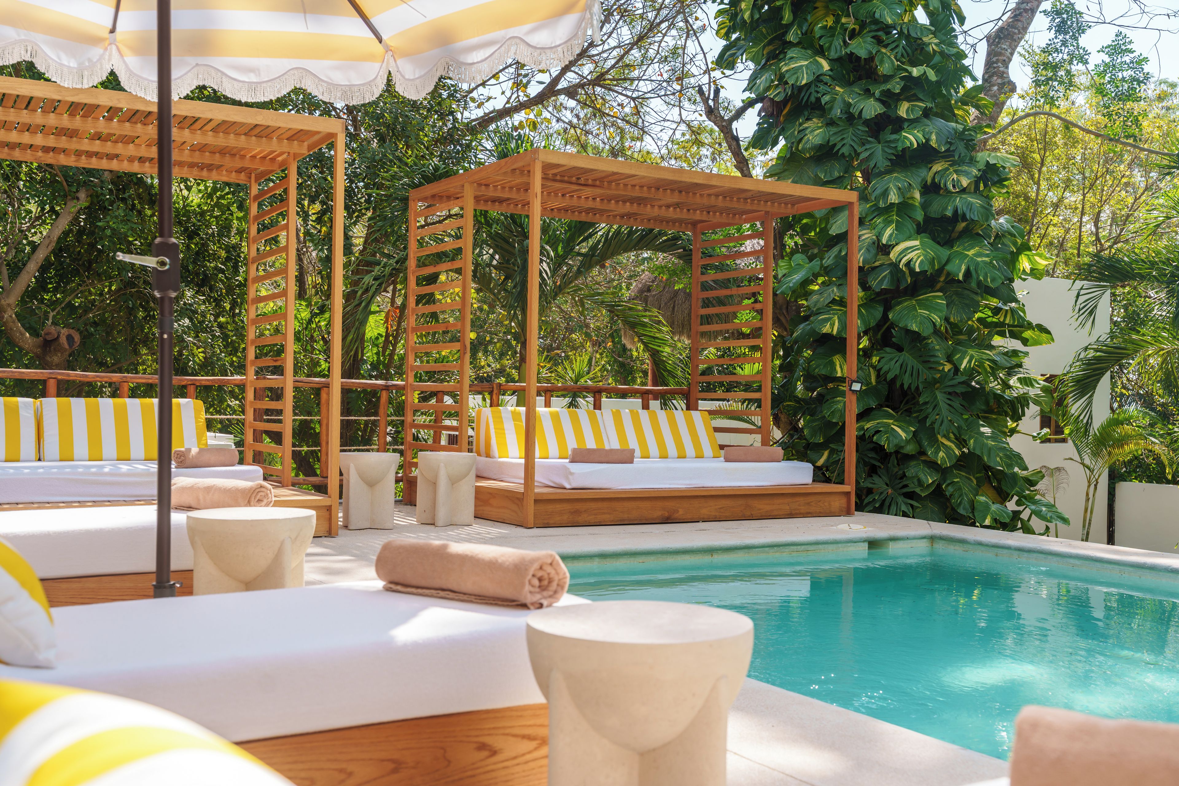 A poolside area with wooden cabanas, striped cushions, and a clear pool.