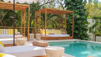 A poolside area with wooden cabanas, striped cushions, and a clear pool.