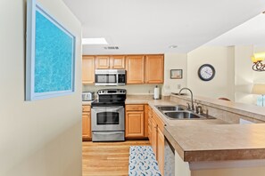 A modern kitchen with wooden cabinets, stainless steel appliances, a double sink, and a clock on the wall.