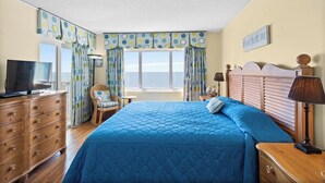 A bedroom with a large bed, a dresser, a television, and a window with curtains.