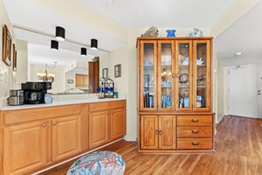Una cocina con armarios de madera, una cafetera y un mueble con puerta de cristal que exhibe objetos decorativos.