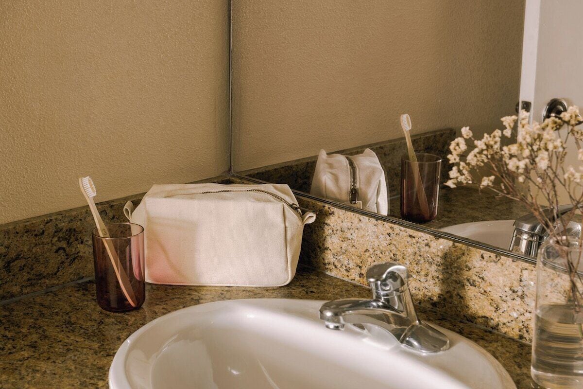 A bathroom with a granite countertop, a white sink, a mirror, a towel, a toothbrush holder, and a vase with flowers.