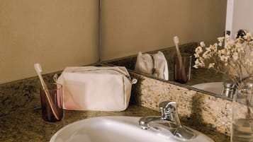 A bathroom with a granite countertop, a white sink, a mirror, a towel, a toothbrush holder, and a vase with flowers.