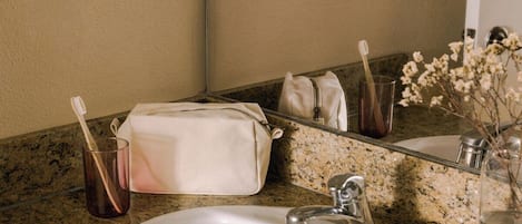 A bathroom with a granite countertop, a white sink, a mirror, a towel, a toothbrush holder, and a vase with flowers.