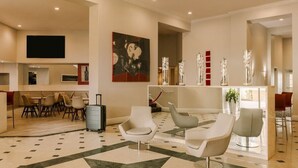 A modern hotel lobby with a geometric patterned floor, contemporary seating, a reception desk, and a large abstract painting.