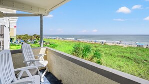A balcony with white chairs overlooking a beach with umbrellas and people.