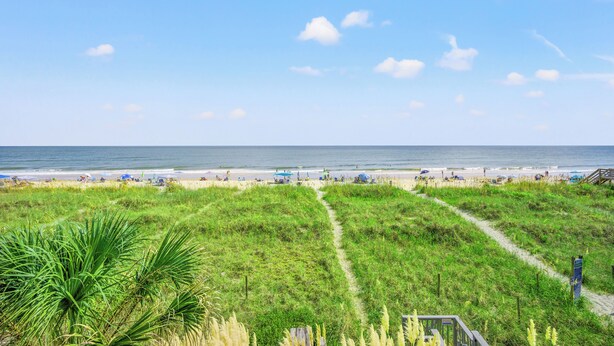 A beach with a grassy path leading to the shore, a boardwalk, and beach umbrellas.