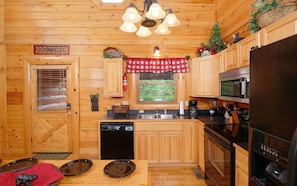 Enjoy cooking in this well-equipped kitchen with appliances, a small window offering a view of the surrounding greenery, and ample storage in the wooden cabinets.