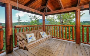 Enjoy a serene view from the deck with a swing set overlooking the lush landscape and distant hills.